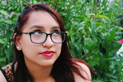 Close-up of thoughtful young woman wearing eyeglasses while looking away against plants