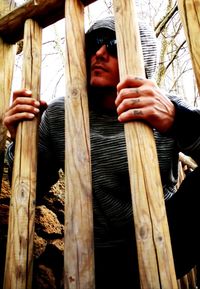 Low angle view of hands holding wood while standing by fence