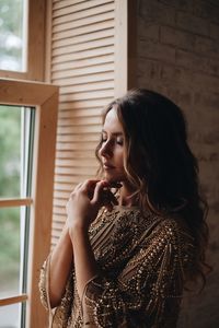 Young woman with eyes closed standing by window at home