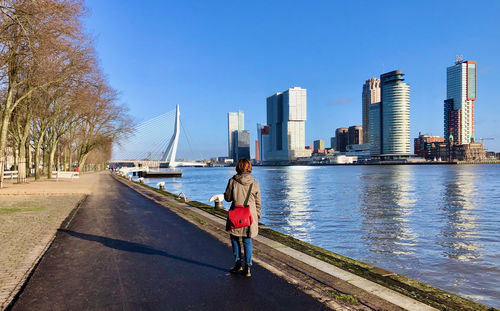 Rear view of woman walking along a riverbank on a clear day with skyline on other side