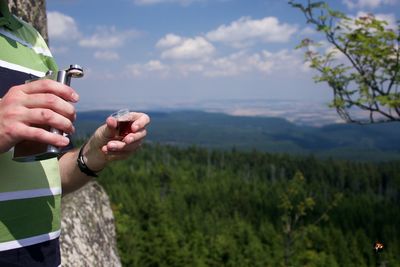 Midsection of man holding hip flask against mountain