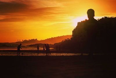 Silhouette of men on shore against sky during sunset