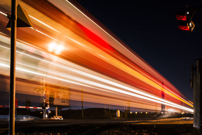 Train light trails on road against sky at night