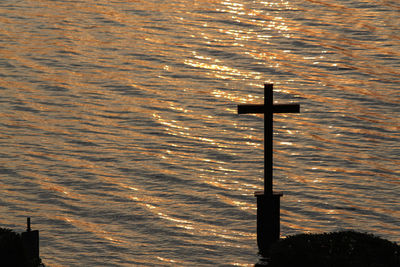 Cross on sea shore against sky during sunset