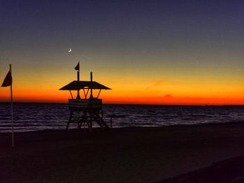 Silhouette lifeguard hut on beach against sky during sunset