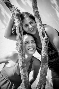 Portrait of two girls between a tree branch against a light blue wall. 