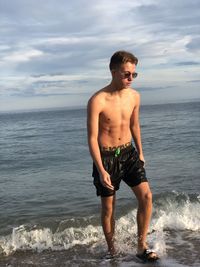 Full length of shirtless man standing at beach against sky