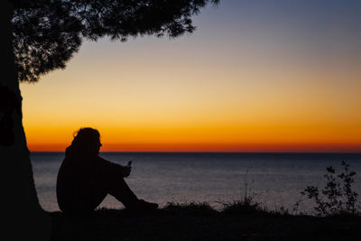 Silhouette man looking at sea against sky during sunset