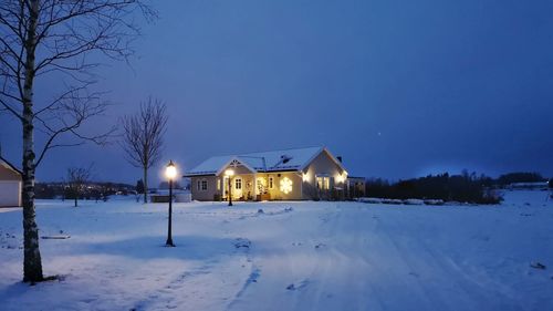 Houses on snow covered field by building against sky at dusk