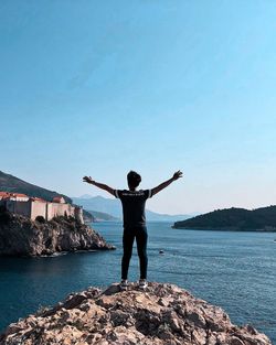 Rear view of man standing on rock by sea against sky