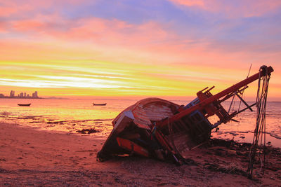 Abandoned boat on beach against sky during sunset