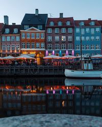 Illuminated buildings by canal against sky at dusk