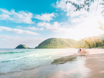 Rear view of people walking at beach against sky