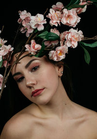 Portrait of woman with pink flowers against black background