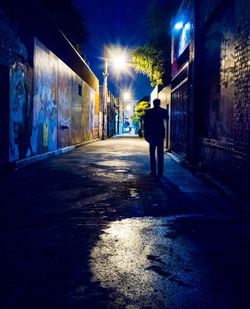 Rear view of man walking on illuminated street at night