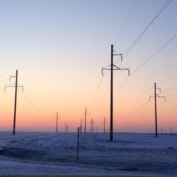 Silhouette electricity pylon by sea against clear sky during sunset