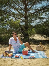 Man eating fruit while sitting on picnic blanket at beach