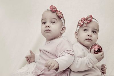 Cute twin baby girls looking away by wall at home during christmas