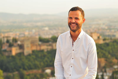 Portrait of smiling young man against city during sunset