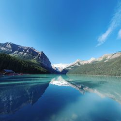 Reflection of mountains on calm lake louise against blue sky