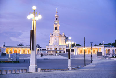 Illuminated street lights in city against sky at dusk