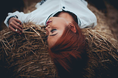 High angle view of young woman lying on hay bale at farm