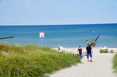 Rear view of men standing on beach against clear sky