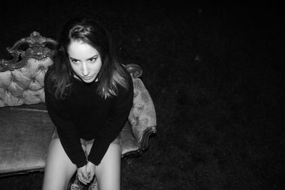 High angle view of thoughtful young woman looking away while sitting on couch outdoors at night