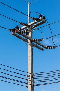 Low angle view of electricity pylon against blue sky