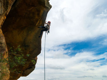 Low angle view of man climbing rock against sky