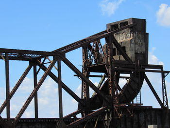 Low angle view of rusty metallic structure against blue sky