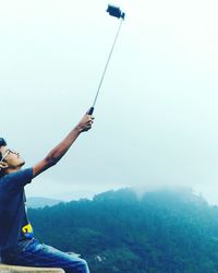 Man taking selfie while sitting on cliff against sky