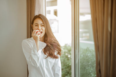 Young woman standing against window at home