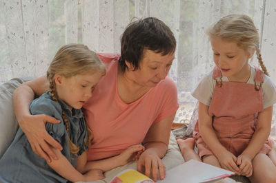 Full length of grandmother with granddaughters reading book at home