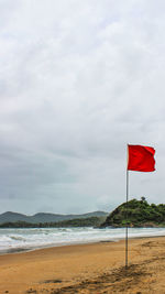 Red flag on beach against sky