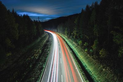 Light trails on road amidst trees against sky at night