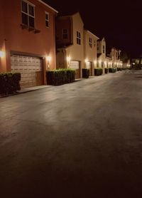 Empty road by illuminated buildings against sky at night