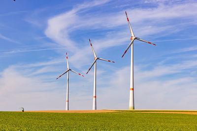 Three wind turbines of different sizes on an agricultural field next to a  small and stunted tree