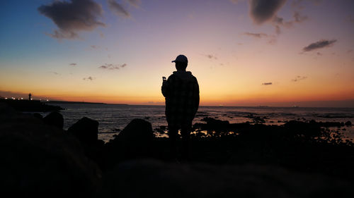 Silhouette man standing on beach against sky during sunset