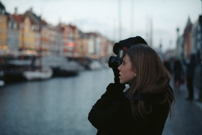 Woman photographing by canal against buildings