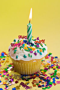 Close-up of cupcake with illuminated candle and confetti