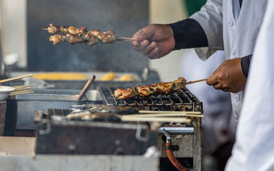 Full frame view of meat on a skewer being cooked with a man's hands