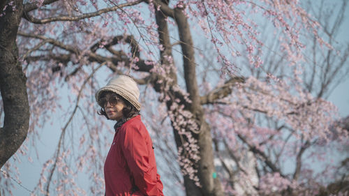 Low angle view of woman standing on cheery blossom tree
