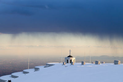 Snow covered buildings against sky during sunset