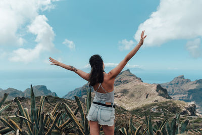 Woman with arms raised standing on mountain against sky