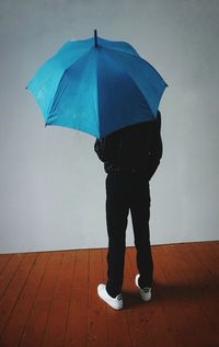 Low section of man holding umbrella standing against wall