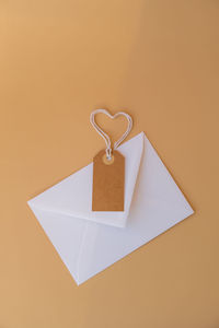 White envelope with beige paper note and rope in heart shape on neutral beige background. greeting