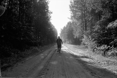 Rear view of man walking on road amidst trees