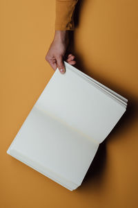 Cropped hand of woman holding book against yellow background