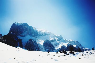 Low angle view of snowcapped mountains against clear blue sky